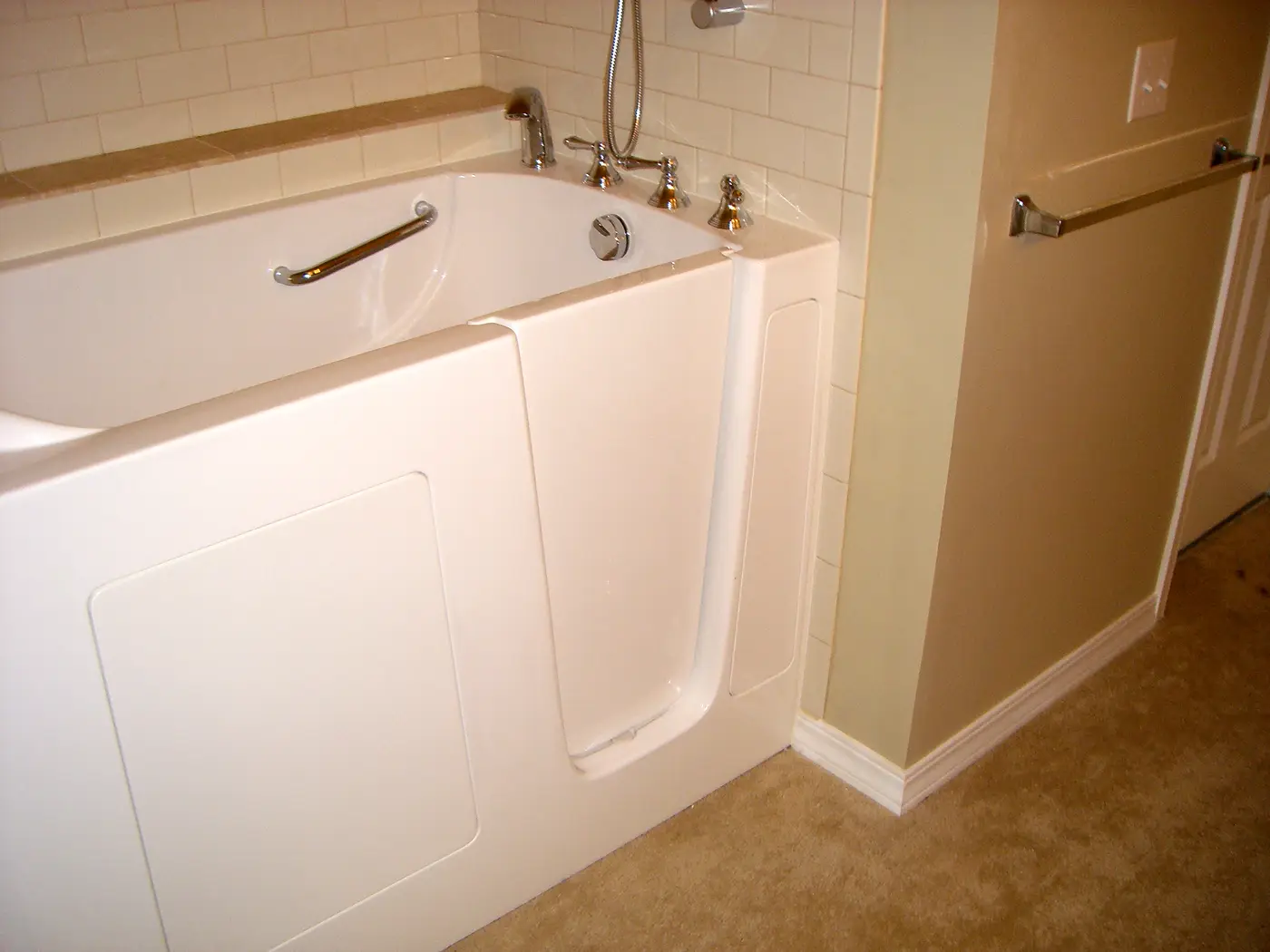 A white walk-in bathtub with its side door closed, a grab bar inside the tub and a handheld shower above the faucet.